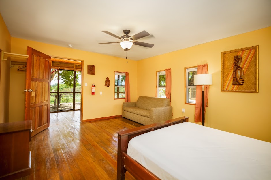 Room at Carmelita River Cabins with wooden floor, ceiling fan, wall painting, and bed facing an open door to the veranda
